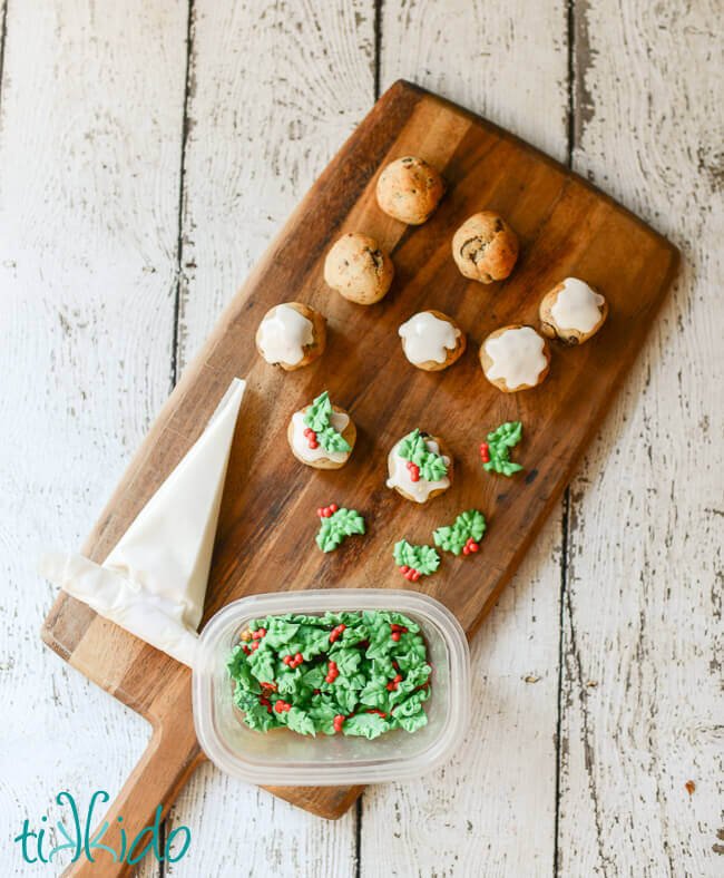 Baked Figgy Pudding Cookies being decorated with rum glaze and sprigs of royal icing holly.