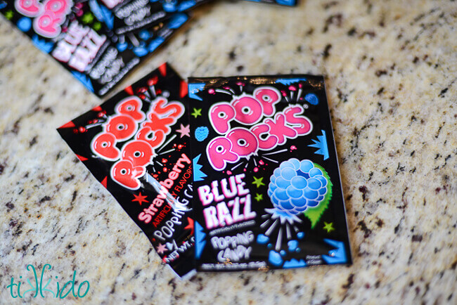 Two packages of pop rocks on a granite surface.