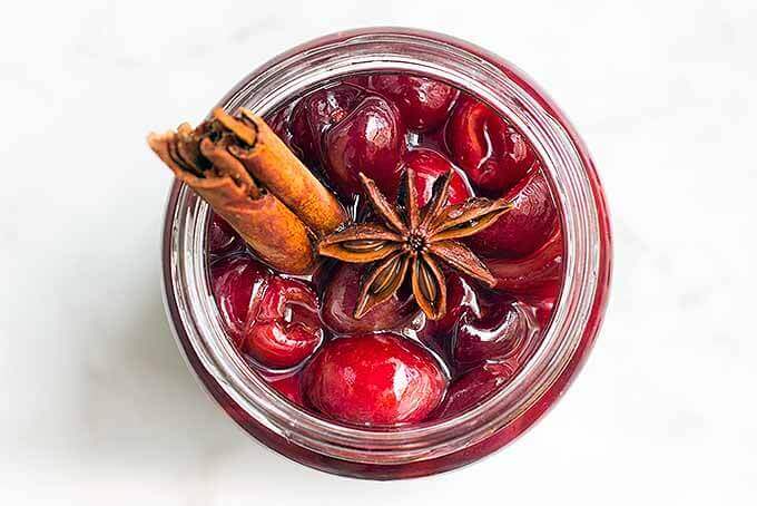Homemade maraschino cherries in a glass jar, garnished with a cinnamon stick and star anise pod.