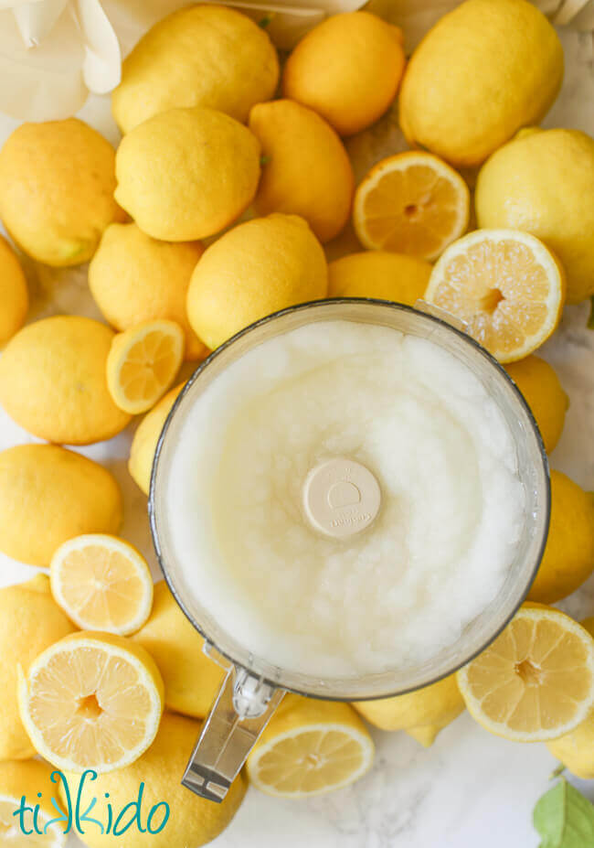 Blended frozen lemonade in a food processor bowl, on top of whole and cut lemons.