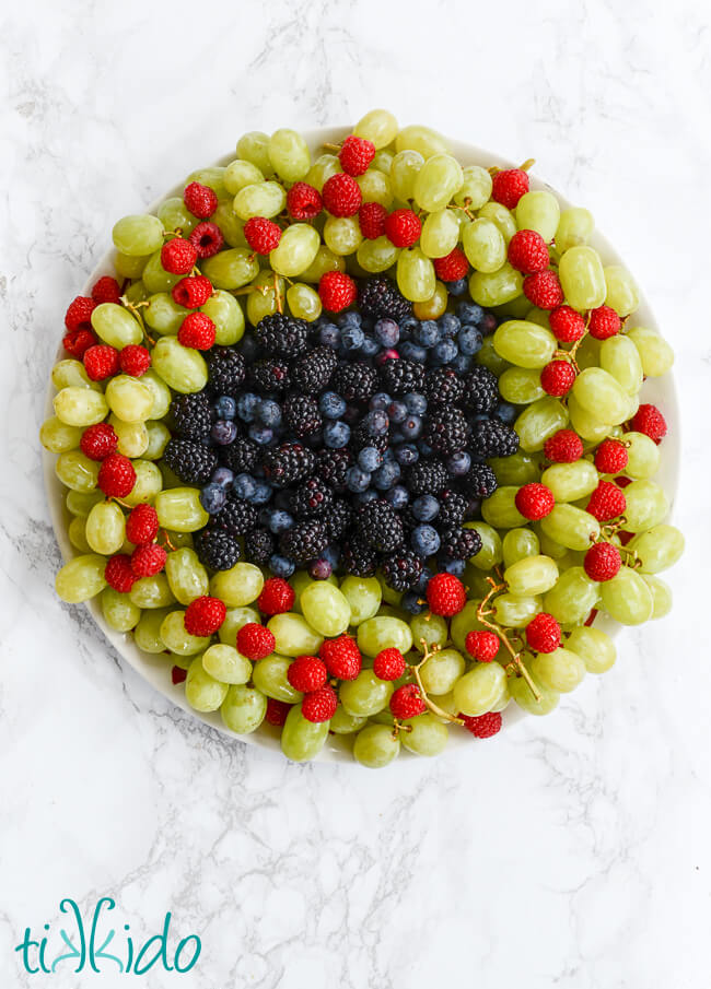 Christmas Fruit Tray that looks like a Christmas wreath, made from green grapes, raspberries, blackberries, and blueberries.