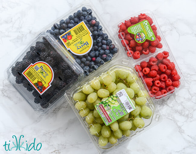 Green grapes, blueberries, blackberries, and raspberries on a white marble surface.
