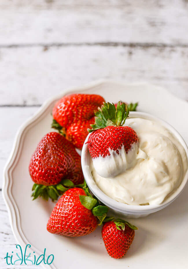 Fruit dip in a bowl, with a strawberry dipped in the fruit dip, and more strawberries surrounding the bowl.