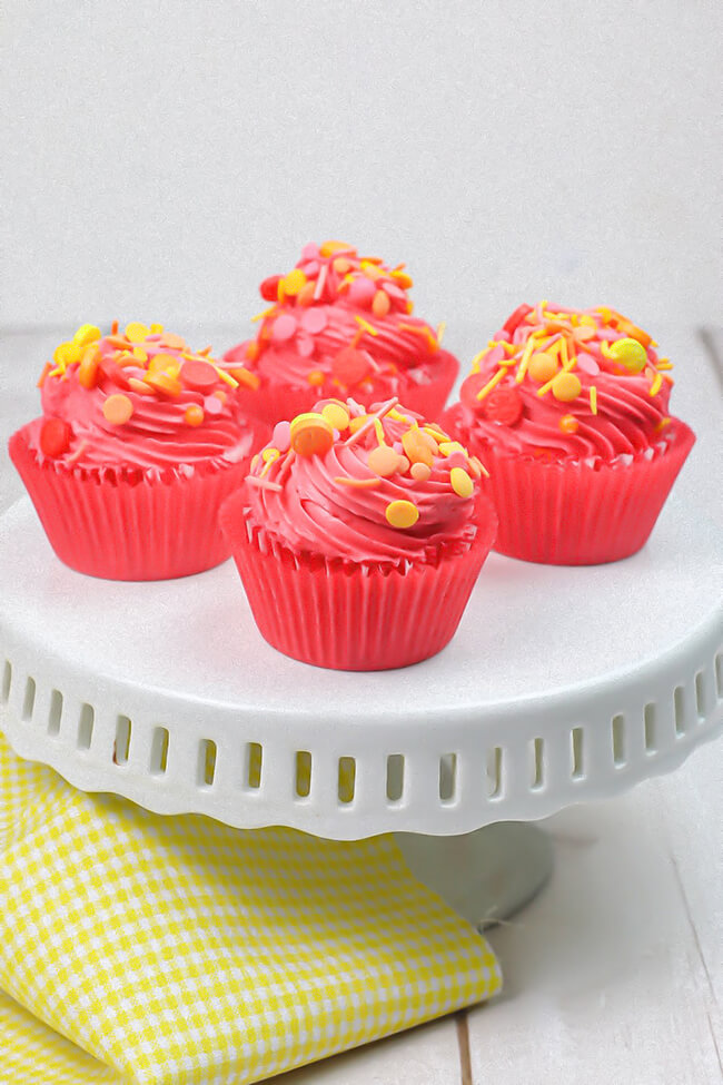 Bright pink Fruit Punch cupcakes on a white cake plate.