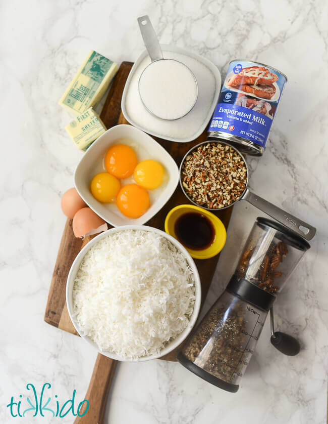 Ingredients for German Chocolate Cake filling on a wooden cutting board on a white marble surface.