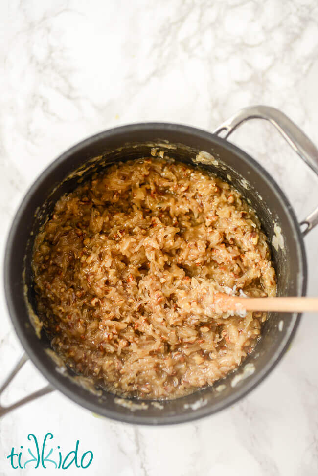 Saucepan filled with German Chocolate Cake filling and wooden spoon, on a white marble background