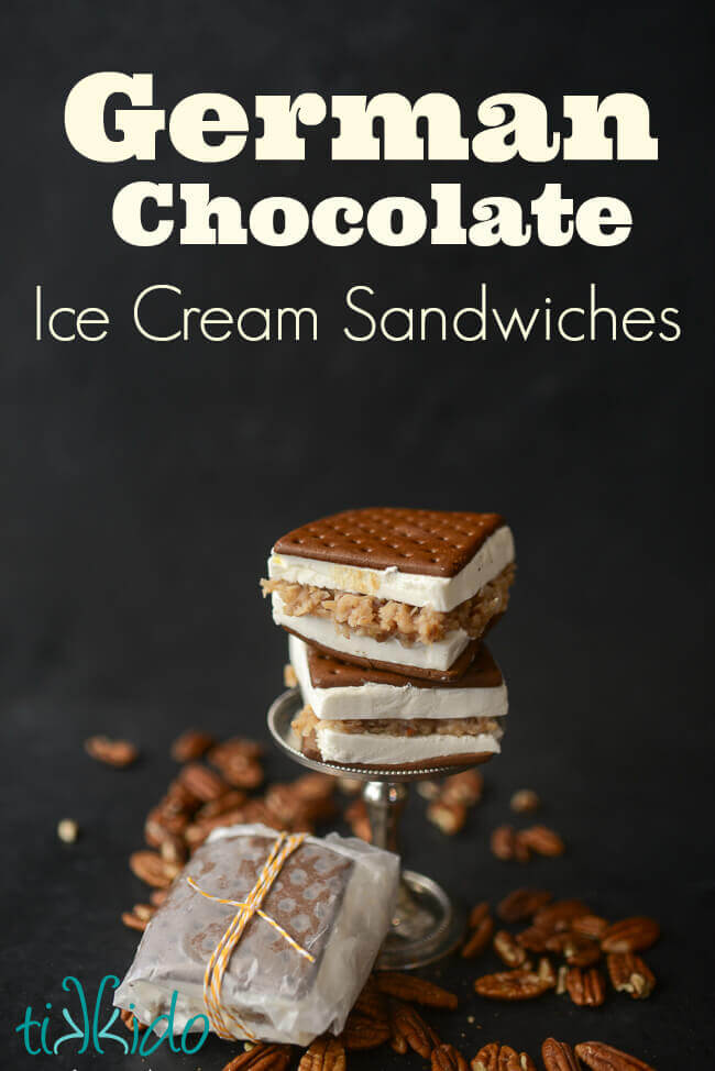 Two ice cream sandwiches filled with German chocolate cake filling stacked on a small metal serving tray, another wax paper wrapped sandwich on the surface blow, pecans scattered around.