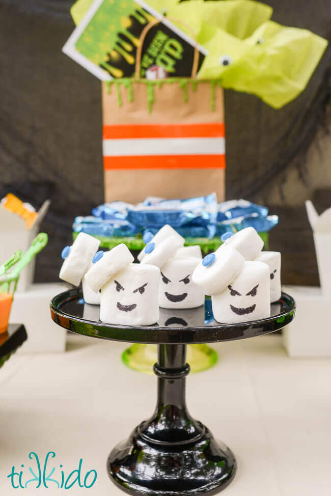 Ghostbusters Stay Puft Marshmallow Treats on a black cake stand on the dessert table at a Ghostbusters Halloween party.