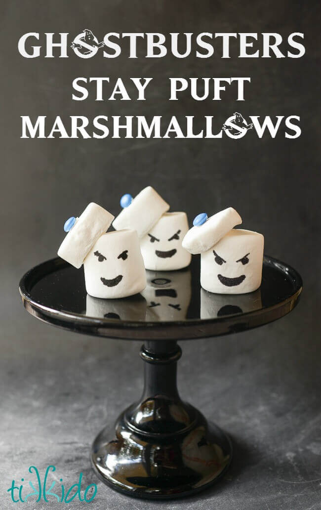Three Ghostbusters Stay Puft Marshmallow Treats on a black glass cake stand, on a black chalkboard background.