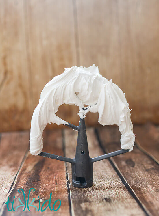 Royal icing covered beater on a wooden table.