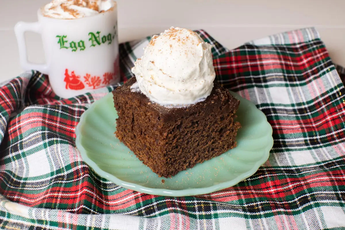 Piece of slow cooker gingerbread cake topped with a scoop of vanilla ice cream on a plaid piece of fabric.