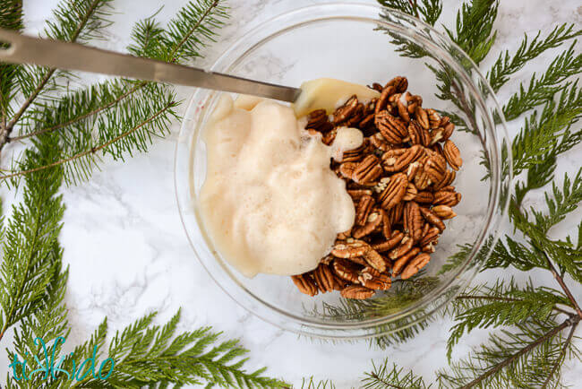 Pecans being mixed with whipped egg whites in a clear bowl to make Gingerbread Spiced Candied Pecans.