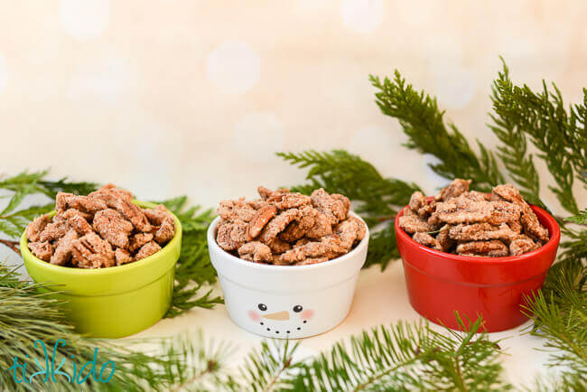 Three small ceramic bowls, red white and green, filled with Gingerbread Spiced Candied Pecans.