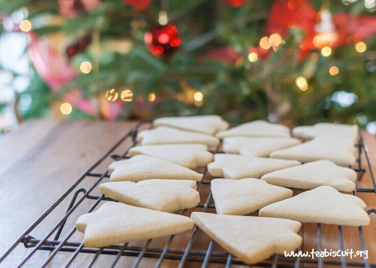 Gluten free cut out sugar cookies cooling on a rack in front of a Christmas tree.