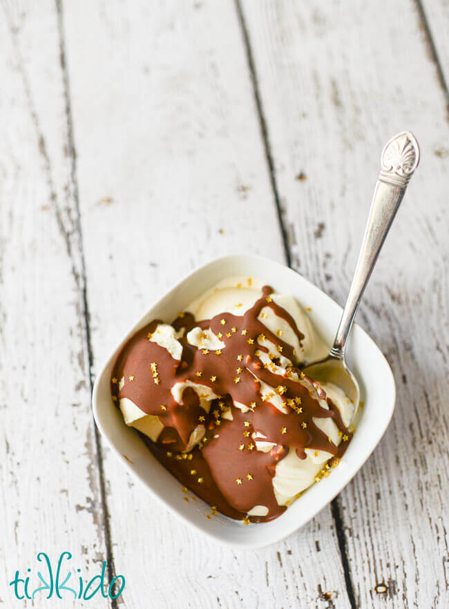 Peanut butter chocolate magic shell ice cream topping covered in edible gold star sprinkles on vanilla ice cream in a white bowl on a white background.