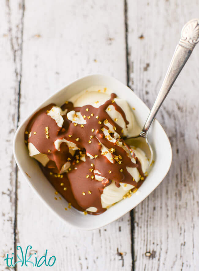 Peanut butter chocolate magic shell ice cream topping covered in edible gold star sprinkles on vanilla ice cream in a white bowl on a white background.