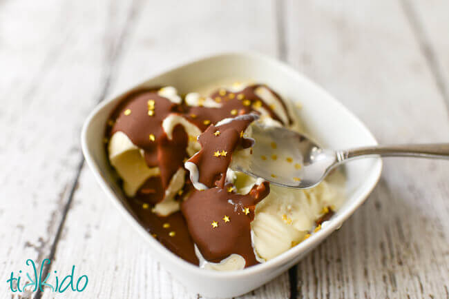 Chocolate peanut butter magic shell ice cream topping on vanilla ice cream in a white bowl, with a spoon cracking the magic shell.