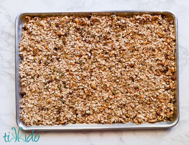 unbaked homemade granola in a sheet pan on a white marble surface.