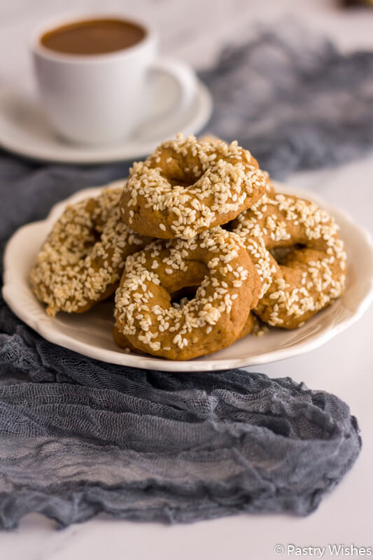 Ladokoouloura, an eggless Greek olive oil cookie, shaped into rings, topped with sesame seeds, and stacked on a plate.