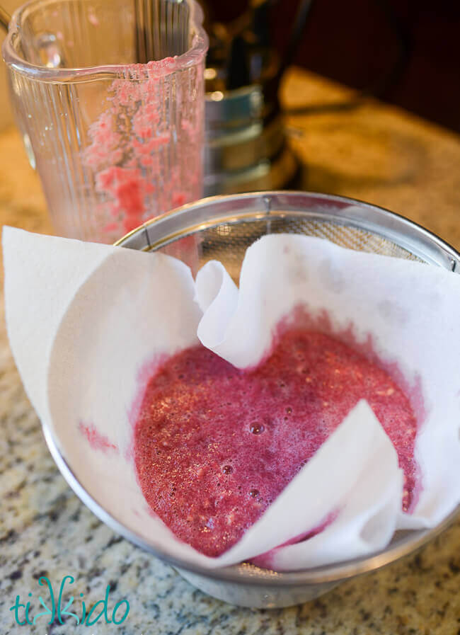 Blended pomegranate seeds being strained through a mesh strainer and cloth.