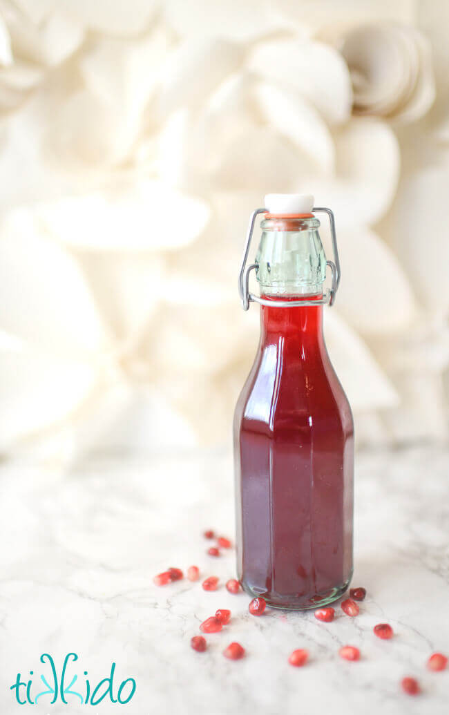 Homemade grenadine in a glass bottle, surrounded by pomegranate seeds