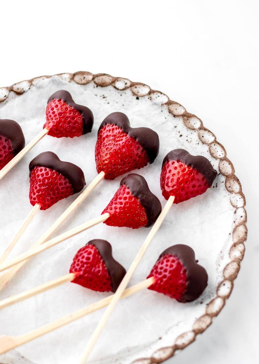 Heart shaped, chocolate covered strawberries on a stick, on a white pottery plate.