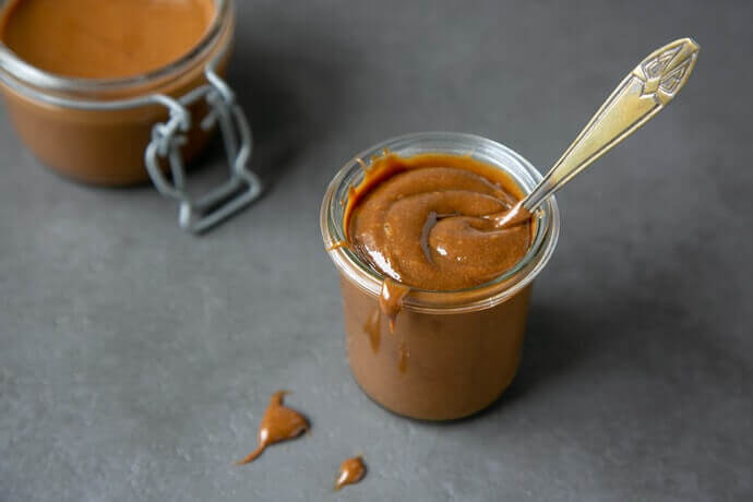 Dulce de leche ice cream topping in a glass jar with a spoon sticking out.