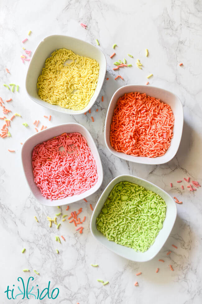 Homemade sprinkles (yellow, orange, pin, and green) in four small, white bowls.