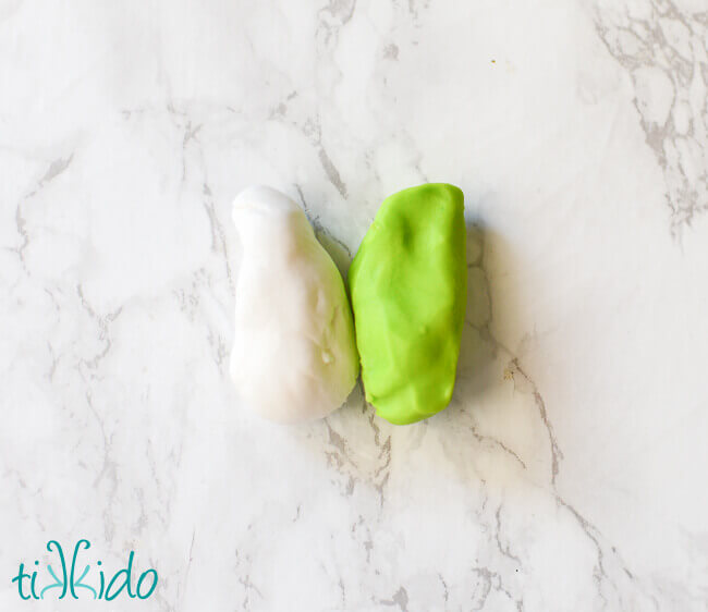 Lump of white gum paste and green chocolate modeling paste on a white marble background.