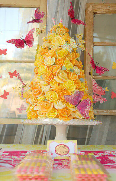 Cake shaped like a tower of yellow fondant roses, surrounded by fluttering pink butterflies.
