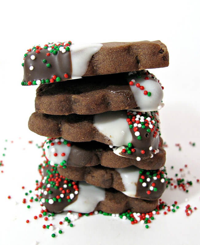 Stack of Chocolate shortbread cookies dipped in chocolate and sprinkled with Christmas sprinkles, on a white background.