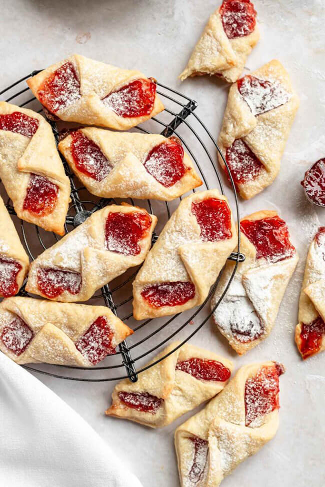 Kolachy cookies filled with jam and sprinkled with powdered sugar on a wire cooling rack.