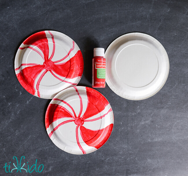 Paper plates being painted with red swirls to look like giant peppermint candies.