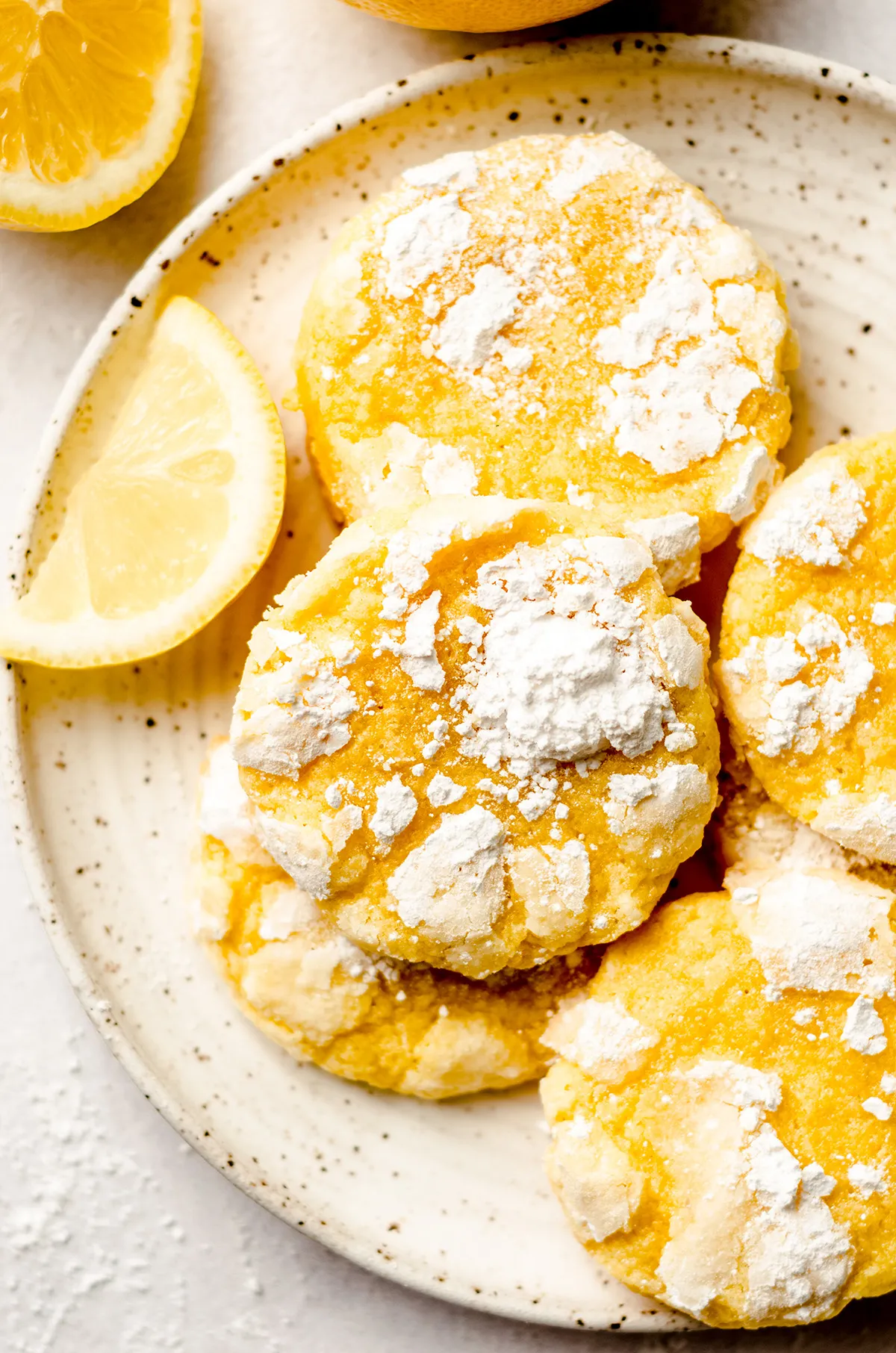 Lemon crinkle cookies stacked on a stoneware plate, next to a wedge of fresh lemon.