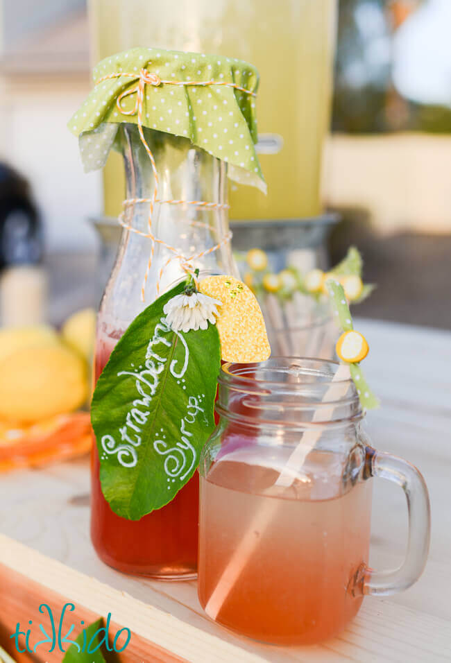 Strawberry simple syrup next to a glass of strawberry lemonade.