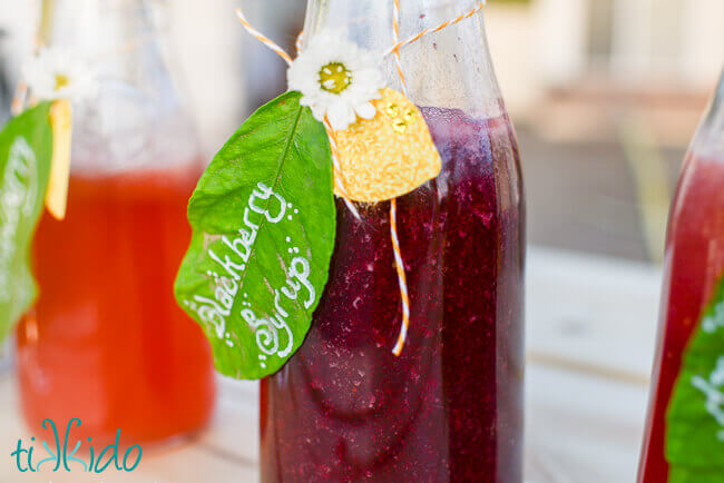 Blackberry syrup in a bottle, labeled with white writing on a real lemon leaf.