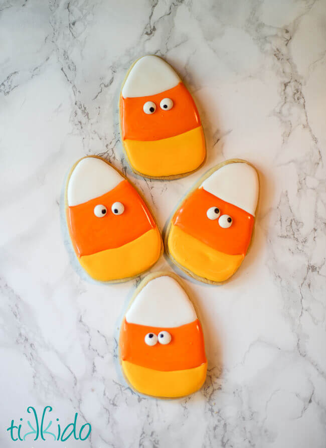 Four candy corn sugar cookies decorated with royal icing and edible googly eyes.