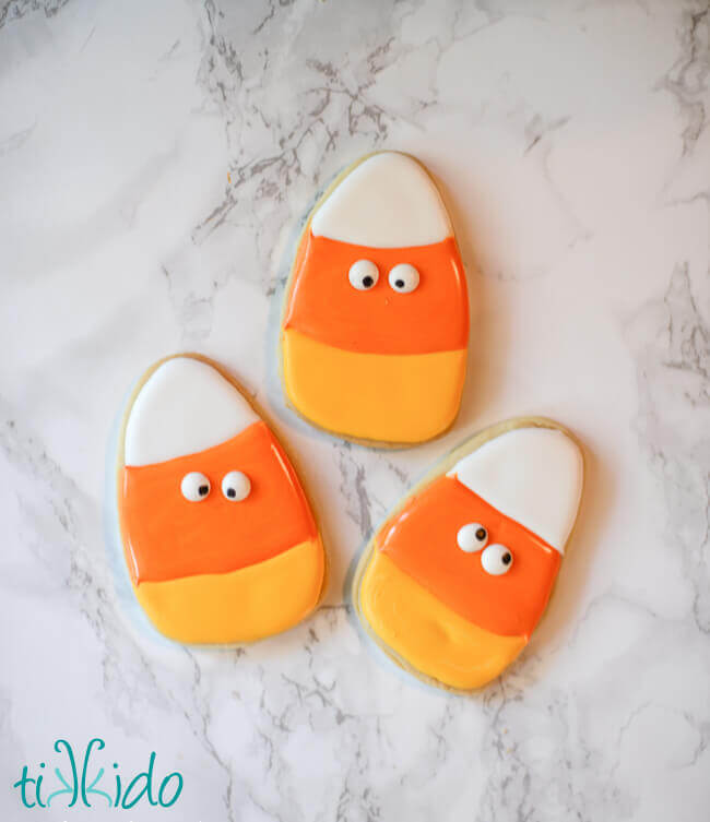 Three candy corn sugar cookies decorated with royal icing and edible googly eyes