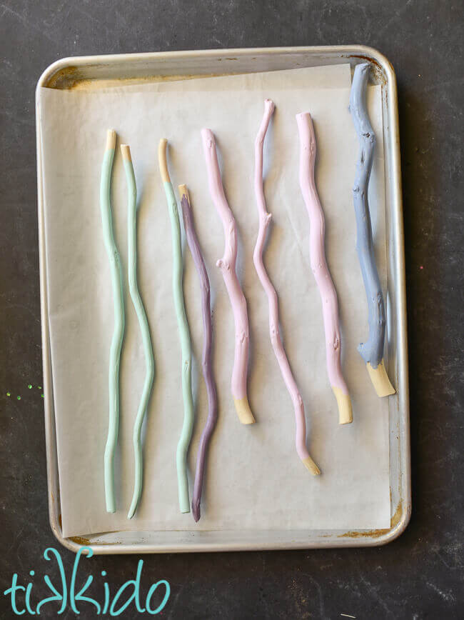 Pastel painted curly willow sticks drying on parchment paper in a sheet pan.