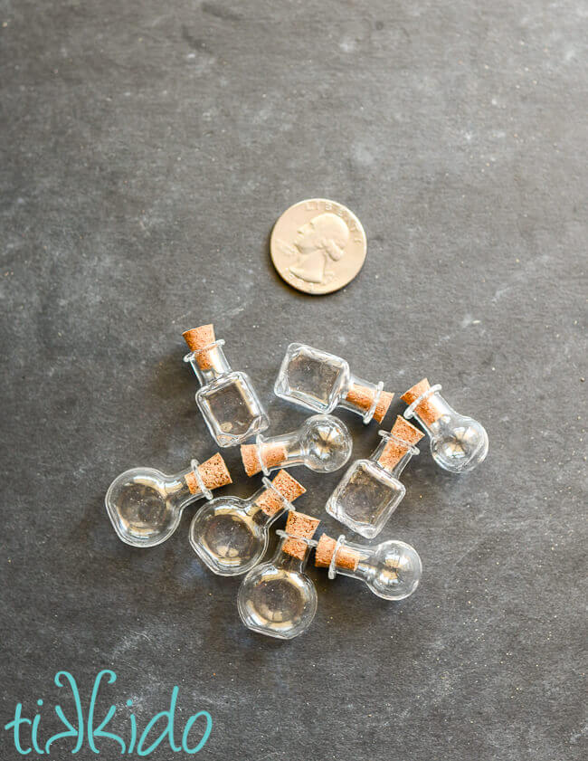 Small glass potion bottles with tiny cork stoppers next to a quarter for scale.