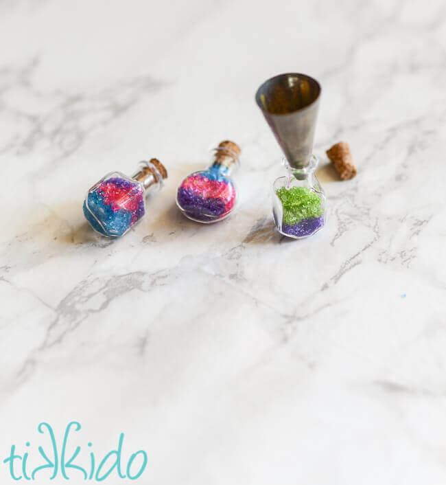tiny glass potion bottles being filled with layers of colored sugar using a cake decorating piping tip as a tiny funnel.