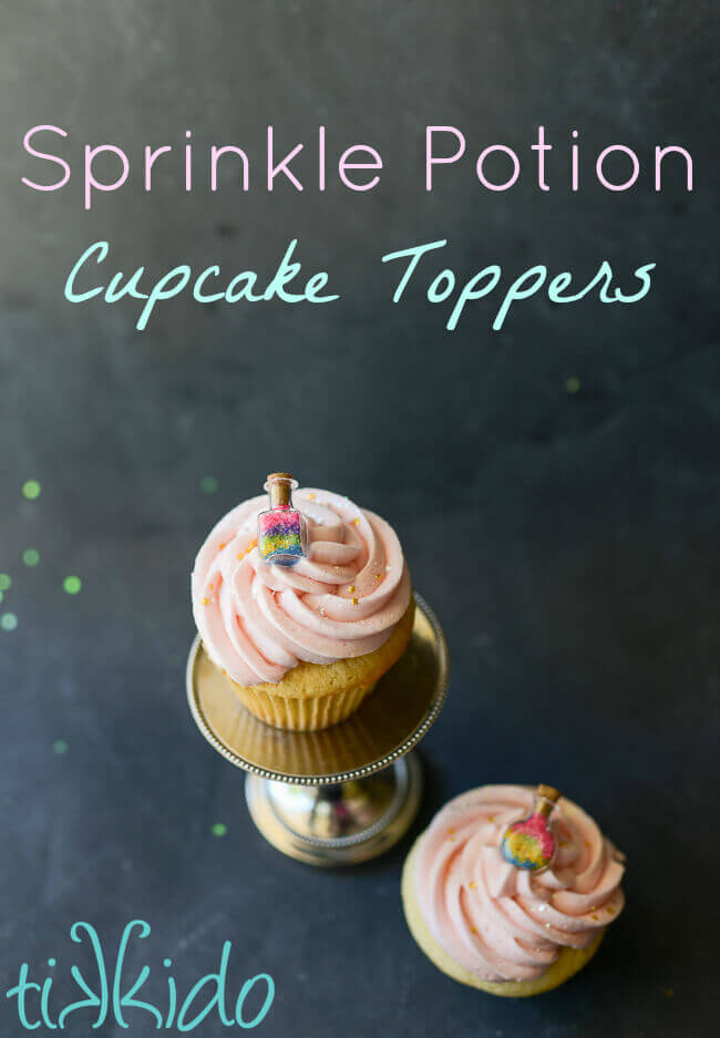 Two vanilla cupcakes topped with light pink icing and a tiny bottle full of multi colored sprinkles.