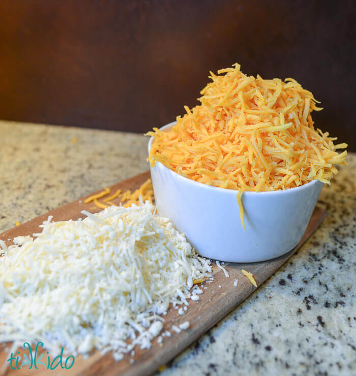 Two types of shredded cheddar cheese on a wooden cutting board.