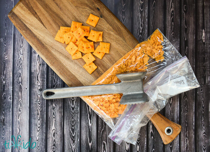 Cheez-its crackers being crushed in a ziplock bag with a kitchen mallet to make a topping for Baked Macaroni and Cheese Recipe.