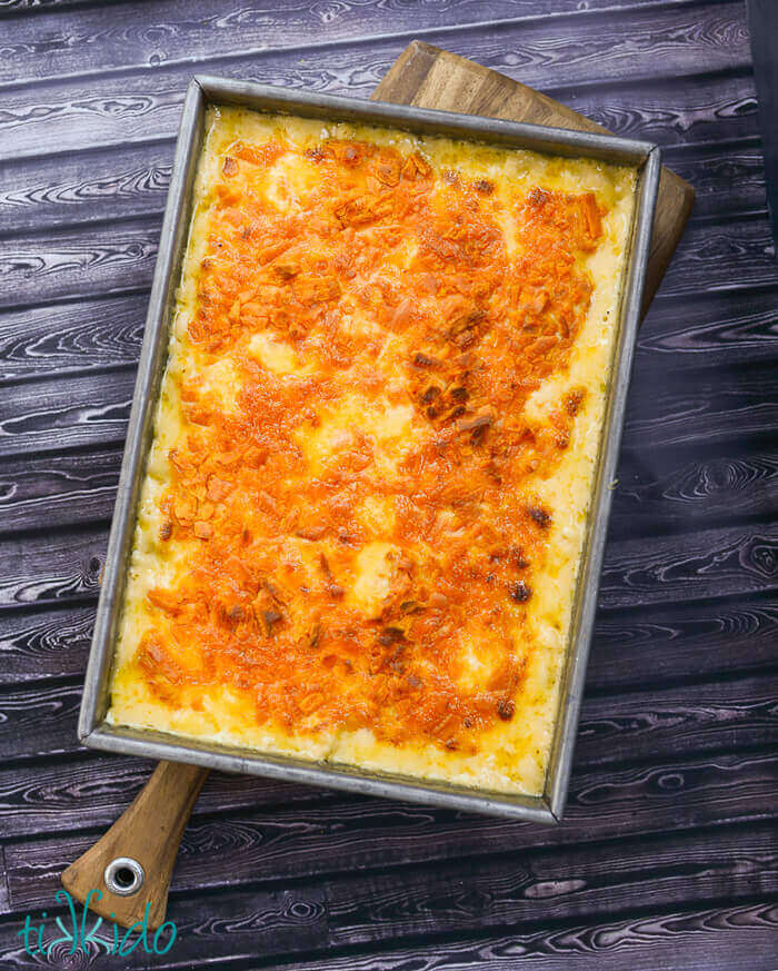 Baked Macaroni and Cheese baked in a 9x13 pan on a wooden cutting board on a dark wood surface.