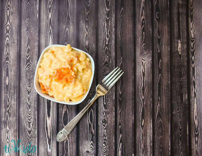Small bowl full of a serving of Baked Macaroni and Cheese next to a fork on a dark wooden surface.