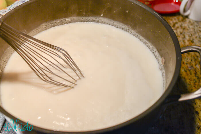 Roux being mixed with milk and stirred with a whisk.