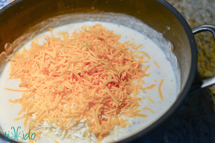 Cheese being added to a pot full of a milk mixture to make Baked Macaroni and Cheese.