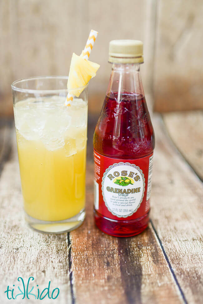 Pineapple and coconut rum cocktail in a tall glass next to a bottle of Rose's Grenadine syrup