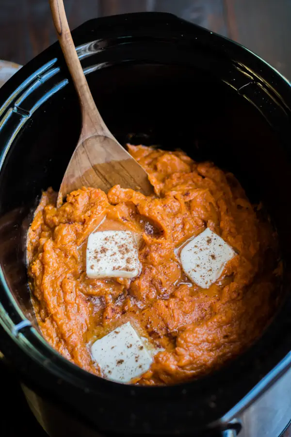 Crockpot mashed sweet potatoes with three pats of butter melting on top.
